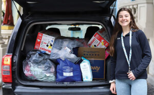 Young woman stands in front of car trunck with donations for Ukraine
