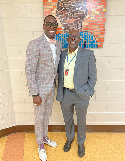 Two men in suits standing in hall of school.