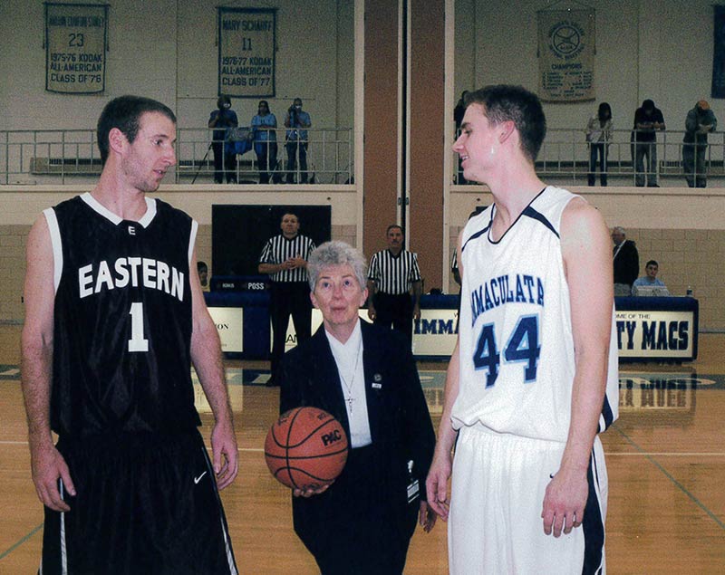 Two males college basketball players waiting for jump ball to be thrown by small woman