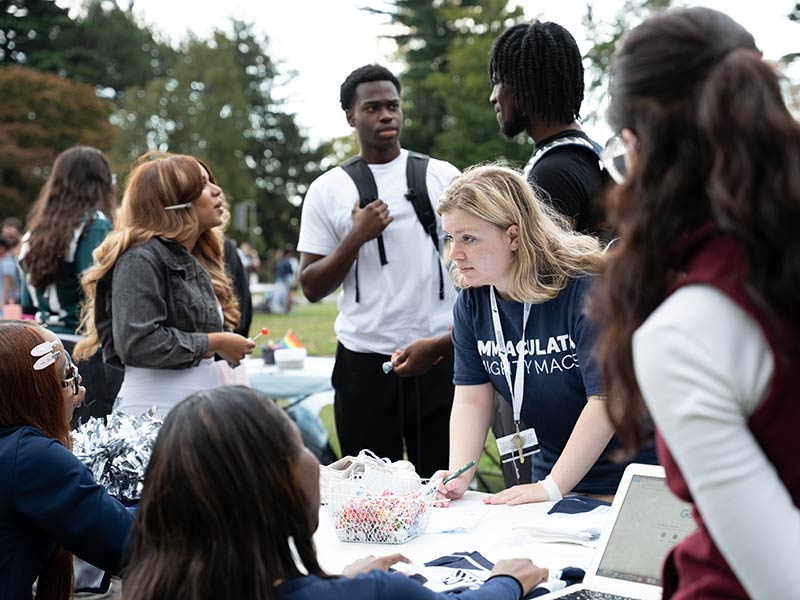 College students standing at table talk to others 