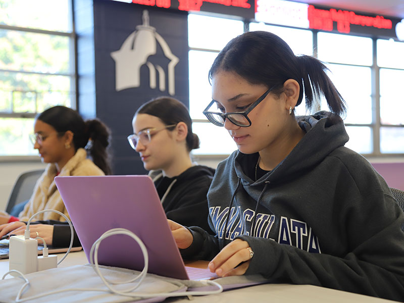Three young women working on laptop computers in classroom
