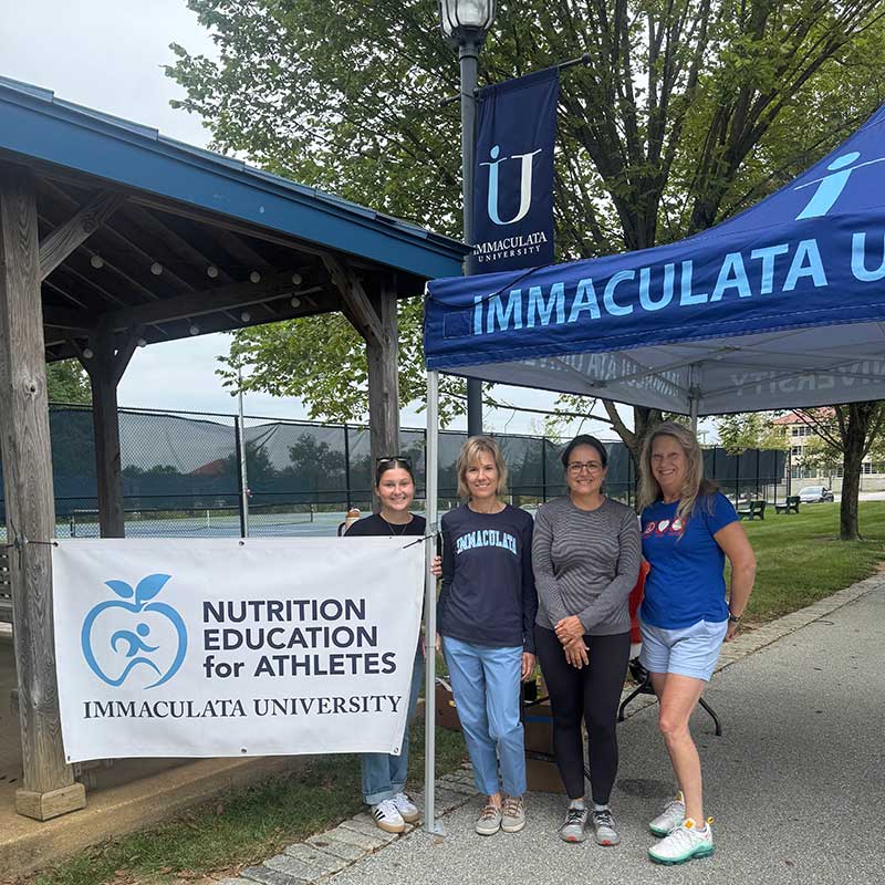 Four women under a tent in front of sign "Nutrition Education for Athletes"