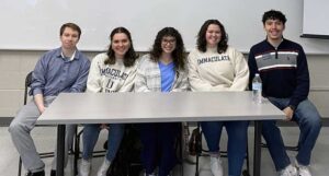 Three young women and two young men sitting behind a table for a panel discussion