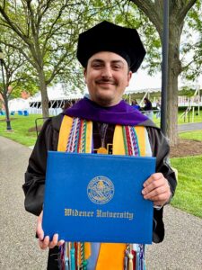 Man in graduation cap and gown holding blue diploma cover with text Widener University