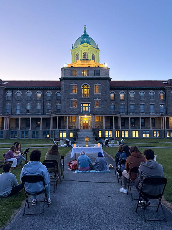 Group of people attending a mass outdoors in the evening in front of an old college building