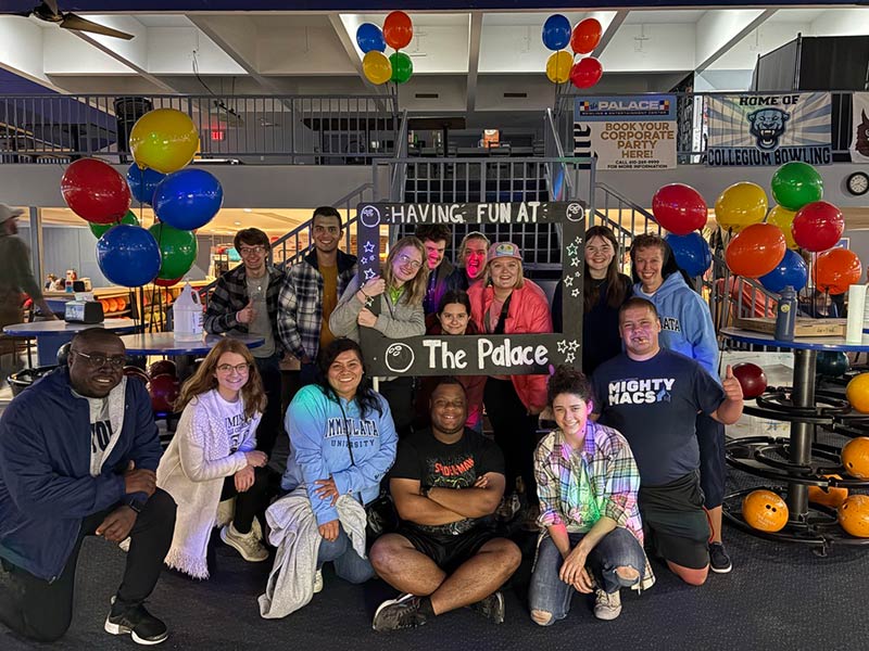 Group of people at bowling alley smiling for the camera, with balloons in the background