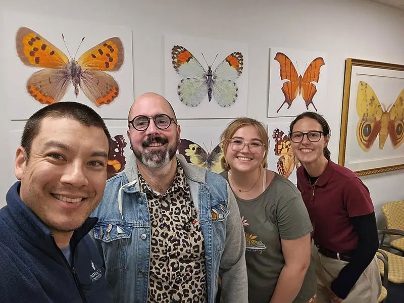 Two men and two young women in front of a wall with illustrations of butterflies