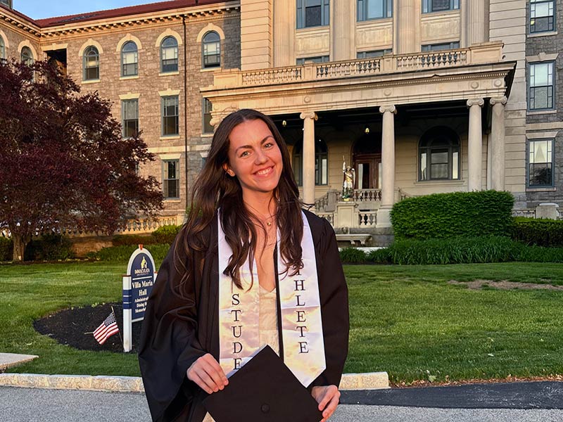 Young woman in cap and gown standing in front of old college building